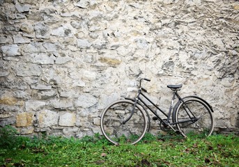 Fototapeta na wymiar Old bike standing on grass in front of old stone wall