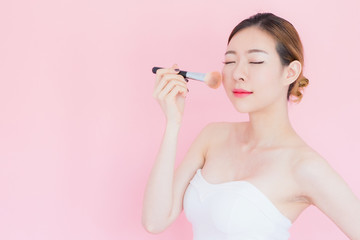asian young beautiful smile woman holding a powder brush over pink background with a copy space