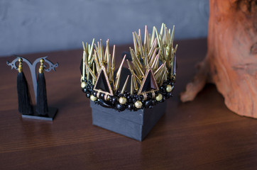 Beautiful gold color fashion crown with black gemstones and thorns. Black earrings with golden diadem on the wooden table