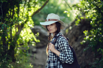 woman traveler with backpack holding hat and looking at amazing mountains and forest, wanderlust travel concept, space for text, atmospheric epic moment