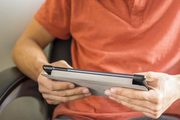 hands typing text information on digital tablet device while sitting at armchair, young man using tablet pc