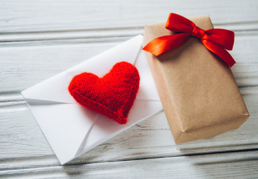 the envelope with the card and a red heart and a gift for his girlfriend in honor of Valentine's day on white wooden background