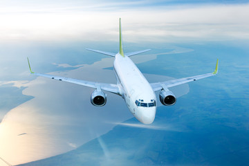 White civil airplane in the sky. Aircraft flying on a high altitude above the plain and the river.