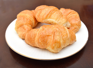 Fresh and tasty croissant in white plate on wood background