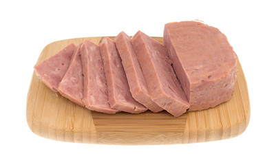 Several thick slices of canned ham on a wood cutting board isolated on a white background side view.