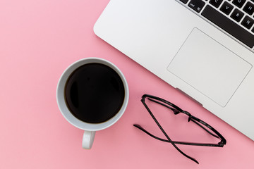 Laptop computer keyboard coffee and reading eyeglasses on bright pink background