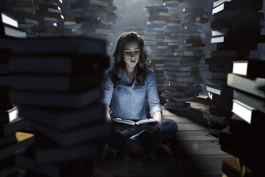 Frau liest zwischen Bücherstapeln