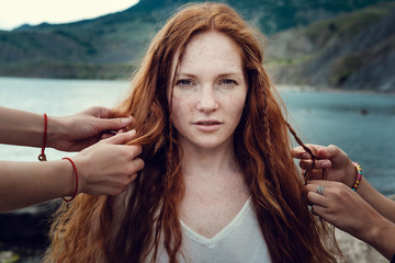 Red-haired girl with hippies with freckles, whose hair is braided by two friends