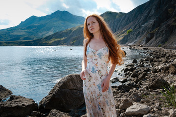 Beautiful boho styled model wearing white dress posing on the beach in sunlight