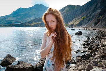 Beautiful boho styled model wearing white dress posing on the beach in sunlight