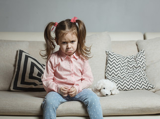 Sad or angry little girl, victim, holding toy dog.