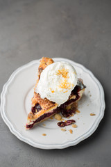 A piece of cherry pie with vanilla ice cream on a white vintage plate on a gray light concrete background. Copy Space. View blank space for text.