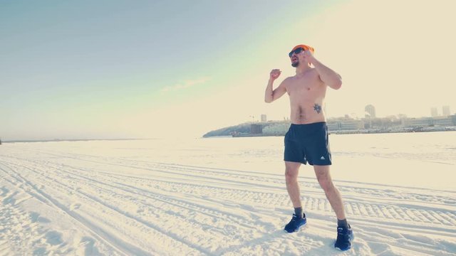 A man in athletic shorts warms up outside in the winter. 