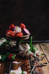 bowl with macarons and strawberries on wooden table with flowers and scissors