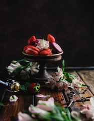 Fototapeta na wymiar bowl with macarons and strawberries on wooden table with flowers and champagne bottle and scissors,