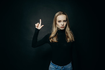 Cute fashionable serius girl. Close up portrait of a young beautiful girl in a turtleneck on a black background in studio. Studio body shot of young female pointing finger up.