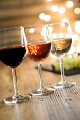 three glass of white red and rose wine with dim light in wooden restaurant table with a grape background