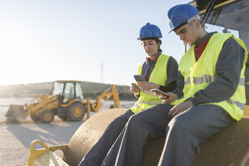 Couple of workers taking a break in their job and looking telephone on steamroller bulldozer