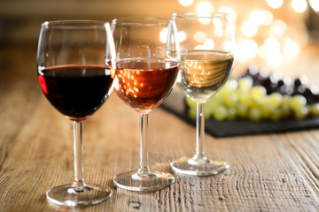 Drei Glas weißer Rot- und Roséwein mit schwachem Licht auf einem hölzernen Restauranttisch mit Traubenhintergrund