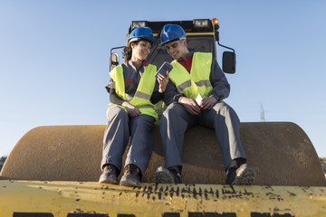 Couple of workers taking a break in their job and looking telephone on steamroller bulldozer