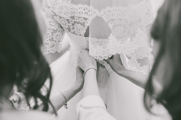 Closeup view of back of bride and female hands of bridesmaids helping bride to get ready for...