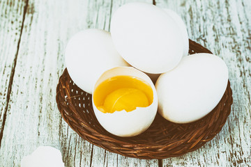 Broke One whole egg amongst white eggs in basket on a white wooden background