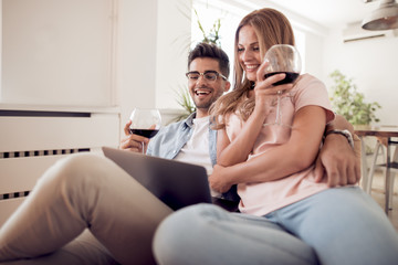 Young couple tasting wine and working on a laptop.