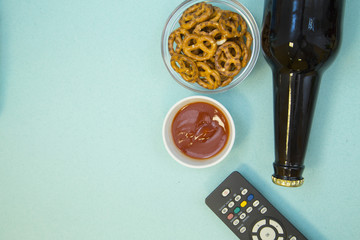 Weekend, Leisure, Lifestyle Concept. Ready to have fun with a remote control, a bottle of beer and pretzel, light blue background, flat lay