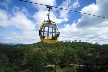 A scenic cable car with colorful cabs over mountains with green forests with blue cloudy sky on the background