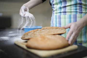 Woman spreading flour in the bowl. Home made integral bread on wooden table. 