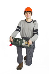 A young man in working grey clothes and orange hard helmet sitting with toolkit on isolated white background.