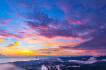 Sunset hidden behind clouds and fog over hills, bright yellow sun on colorful cloudscape, blue violet orange sky. Panorama of the Black Sea coastline from Akhun mountain, Big Sochi, Russia.