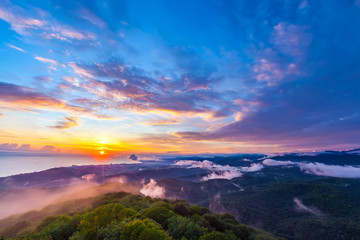 Sunset hidden behind clouds and fog over hills, bright yellow sun on colorful cloudscape, blue violet orange sky. Panorama of the Black Sea coastline from Akhun mountain, Big Sochi, Russia.