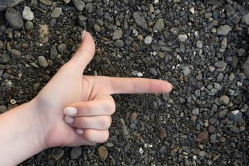 Female hand folded in the sign of the gun lying on the sea pebbles black grey