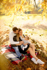 Young family sitting on the ground in autumn park