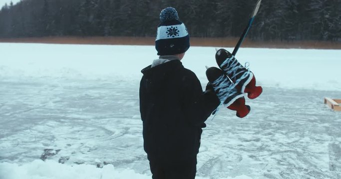 TRACKING Kid walking towards outdoor rink on a frozen lake to play pond hockey. 4K UHD