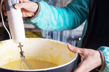 Female hands stirring dough with a mixer for cake or bread in a bowl on a kitchen worktop, preparation for baking.