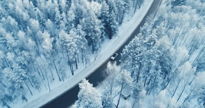 Aerial view of a car driving on a snowy forest road. 4K.