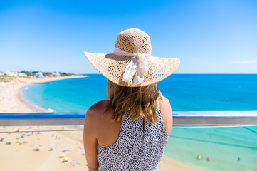 Woman wearing a hat, standing at viewpoint over, Albufeira beach on the Algarve, Portugal