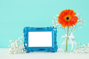 Image of beautiful bouquet of spring flowers next to blank vintage photo frame on wooden table. For photography mock up montage.
