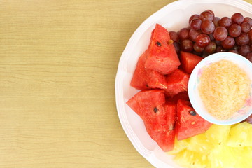 Thai fruits sliced pieces in pink dish (watermelon , grape, pineapple) with spice sauce (sugar, salt and chili) for dip on wooden table, Top view and have copy space for put text