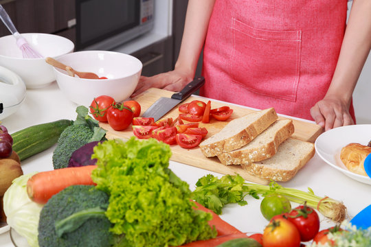 close up of hand cutting tomato on board in kitchen room