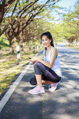 sporty woman sitting on the road in the park and using smartphone with earphone to listening music