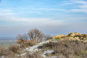 Rocks on top of a hill. The slopes of the hill are covered with shrubs and trees. Autumn day.