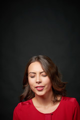 Woman in red shirt and wavy hair making a wish with closed eyes, over dark background, blank copy space above