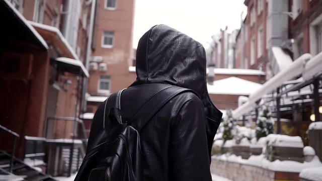 bearded mysterious man walks through an abandoned old town in the snow day back to the camera. dressed in black leather clothes