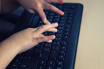 Little girl sitting at the computer and she writes on the keyboard.