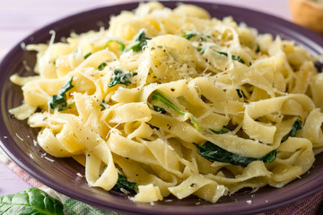 Tagliatelle pasta with spinach, garlic and Parmesan cheese on purple wooden background.