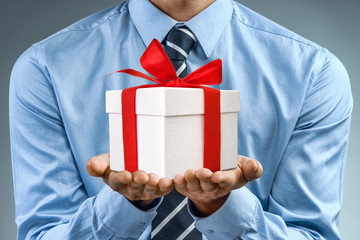 Man in blue shirt holding white gift box with red ribbon. Close up. Business concept