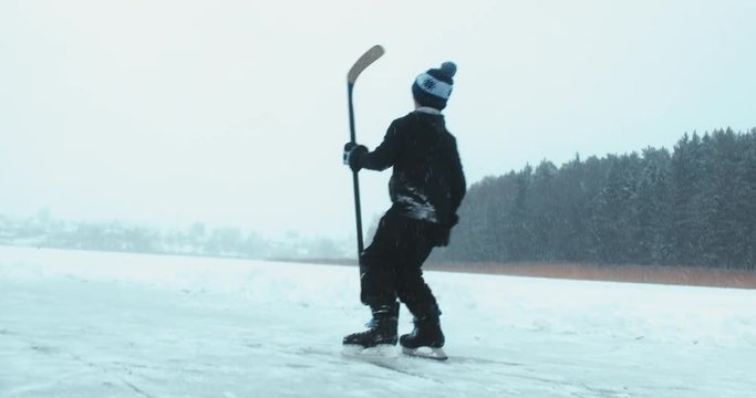 Kid celebrates after scoring a goal in pond hockey game on a frozen lake ice surface. 4K UHD